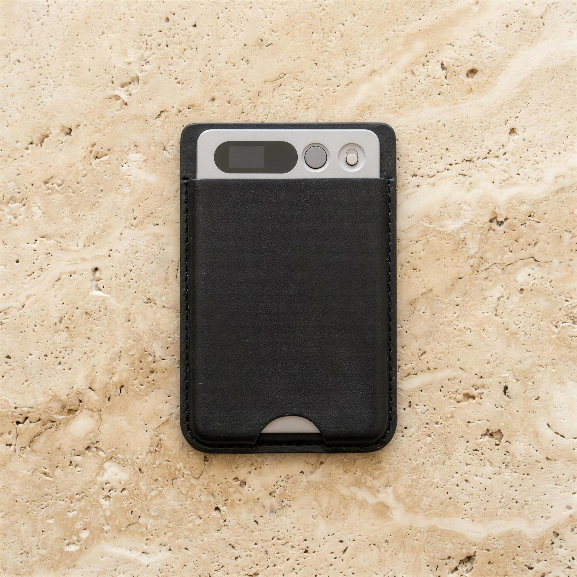 notu R1 Pro in its black leather MagSafe wallet lying on travertine stone — display window, record button and microphone visible on the aluminum top edge