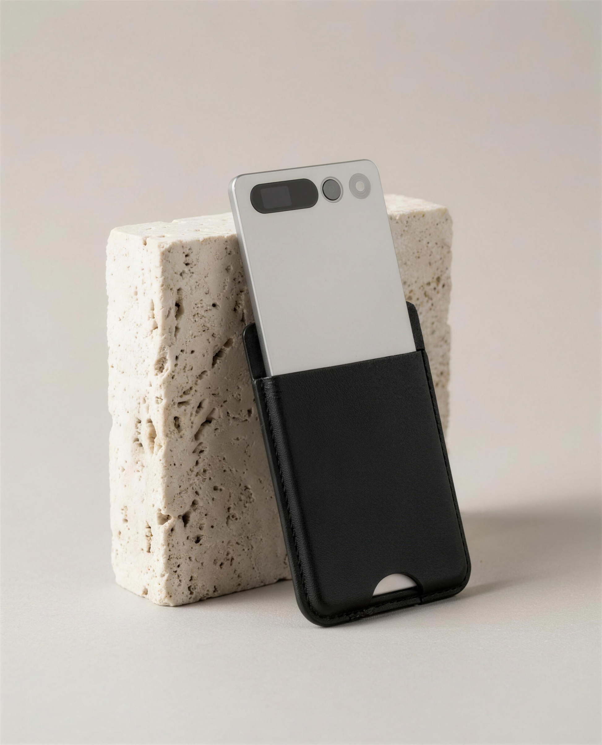 notu R1 Pro — matte silver aluminum recorder card half-drawn from its black leather MagSafe wallet, leaning against a travertine stone block