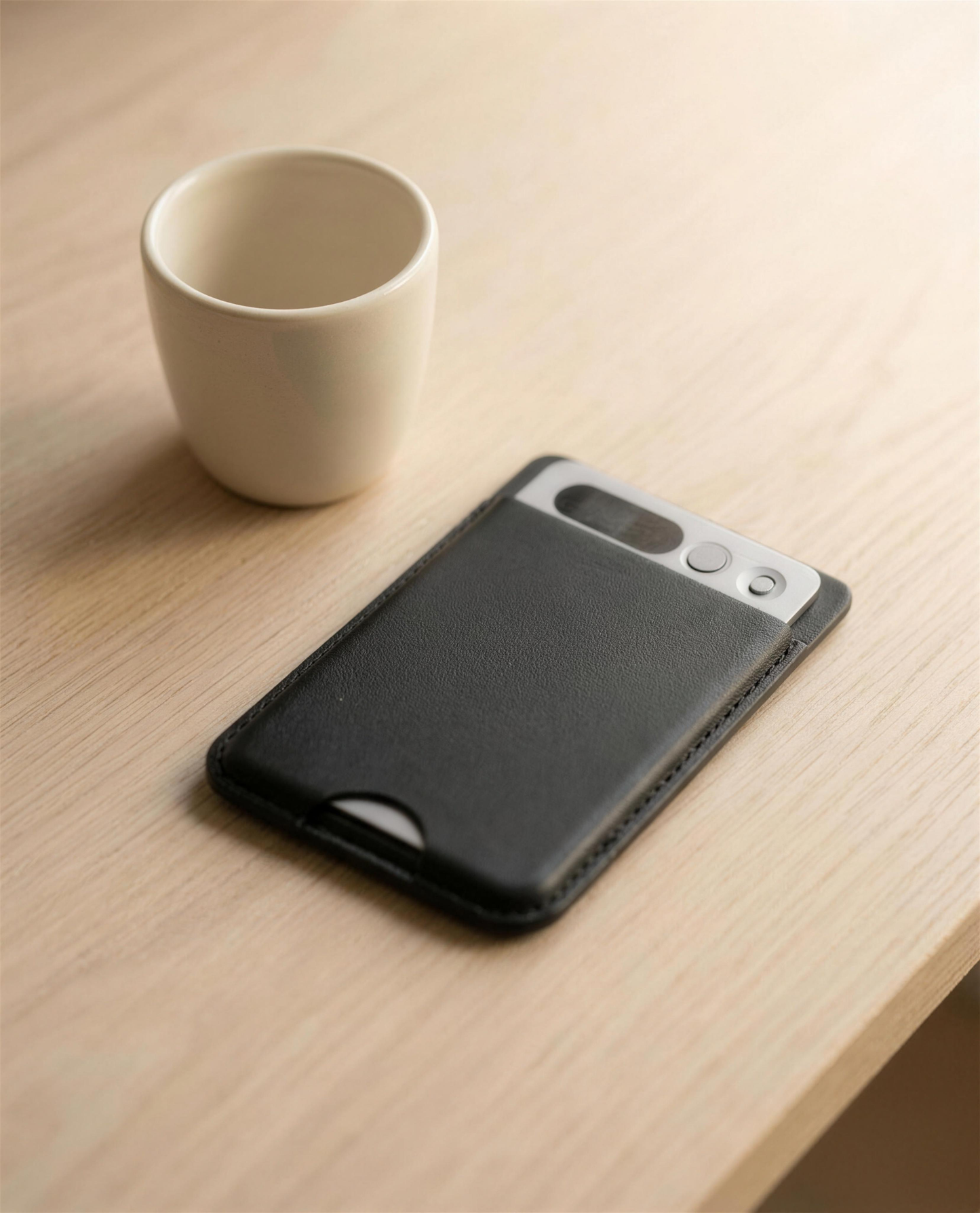 notu R1 Pro in its black leather MagSafe wallet on an oak desk next to a ceramic espresso cup